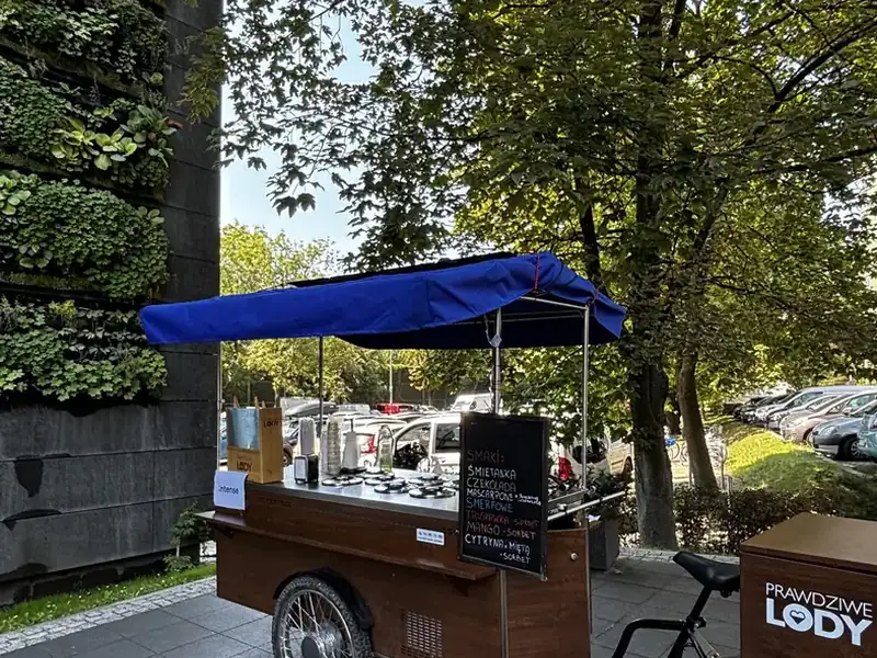 Rower z lodami Prawdziwe Lody z tablicą smaków przy zielonej ścianie biurowca w Krakowie